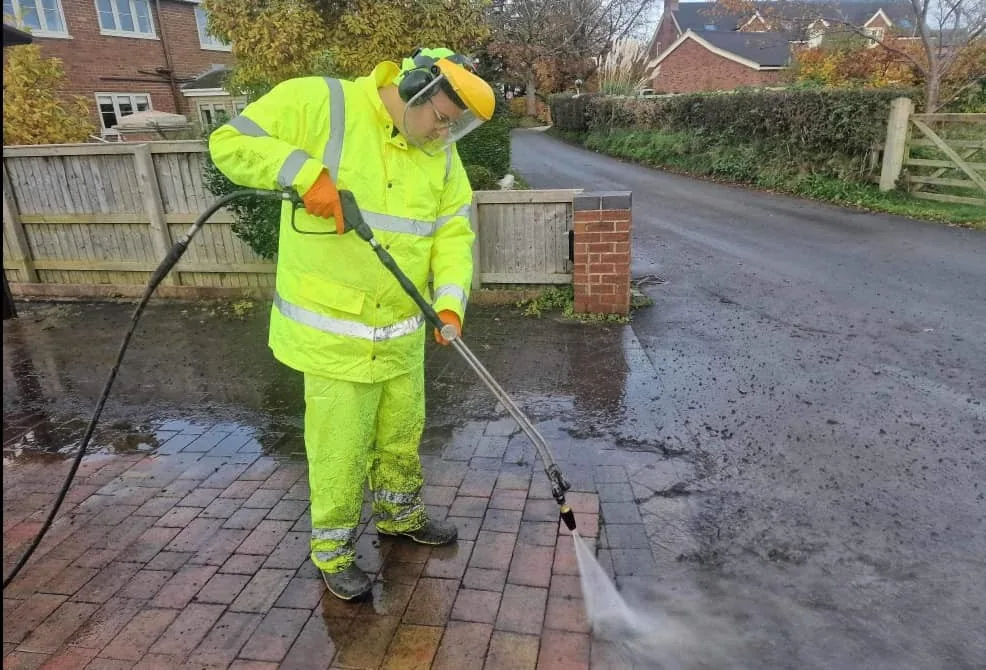 Worker in high-visibility clothing pressure washing a driveway